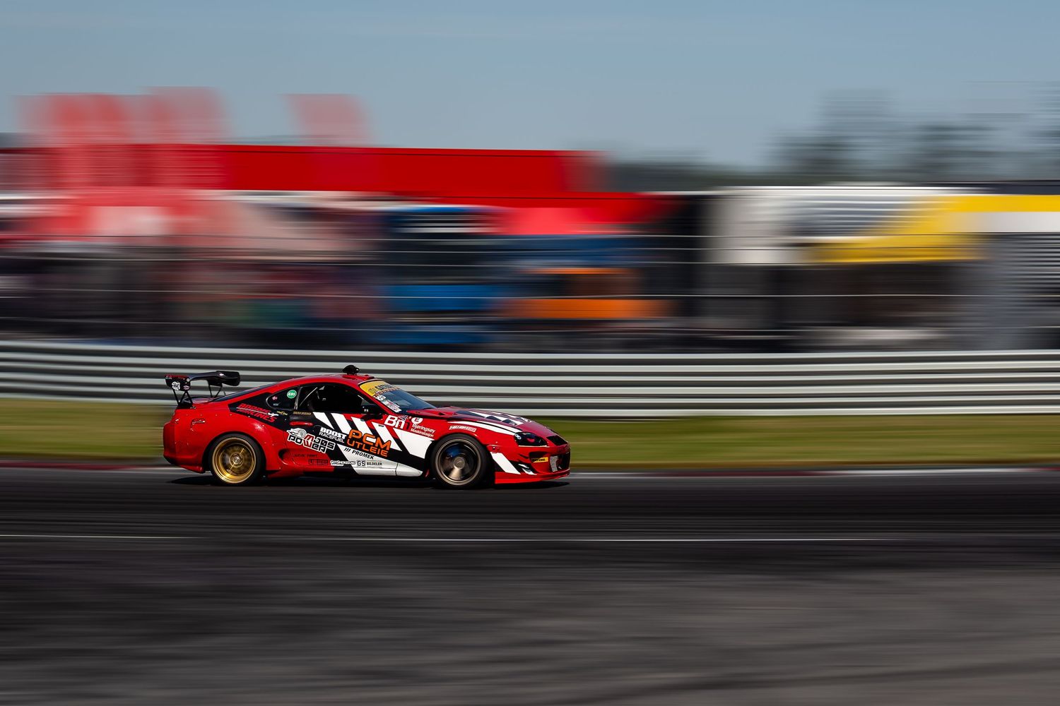 Red race car speeds down racetrack with motion blur effect creating dynamic racing atmosphere.