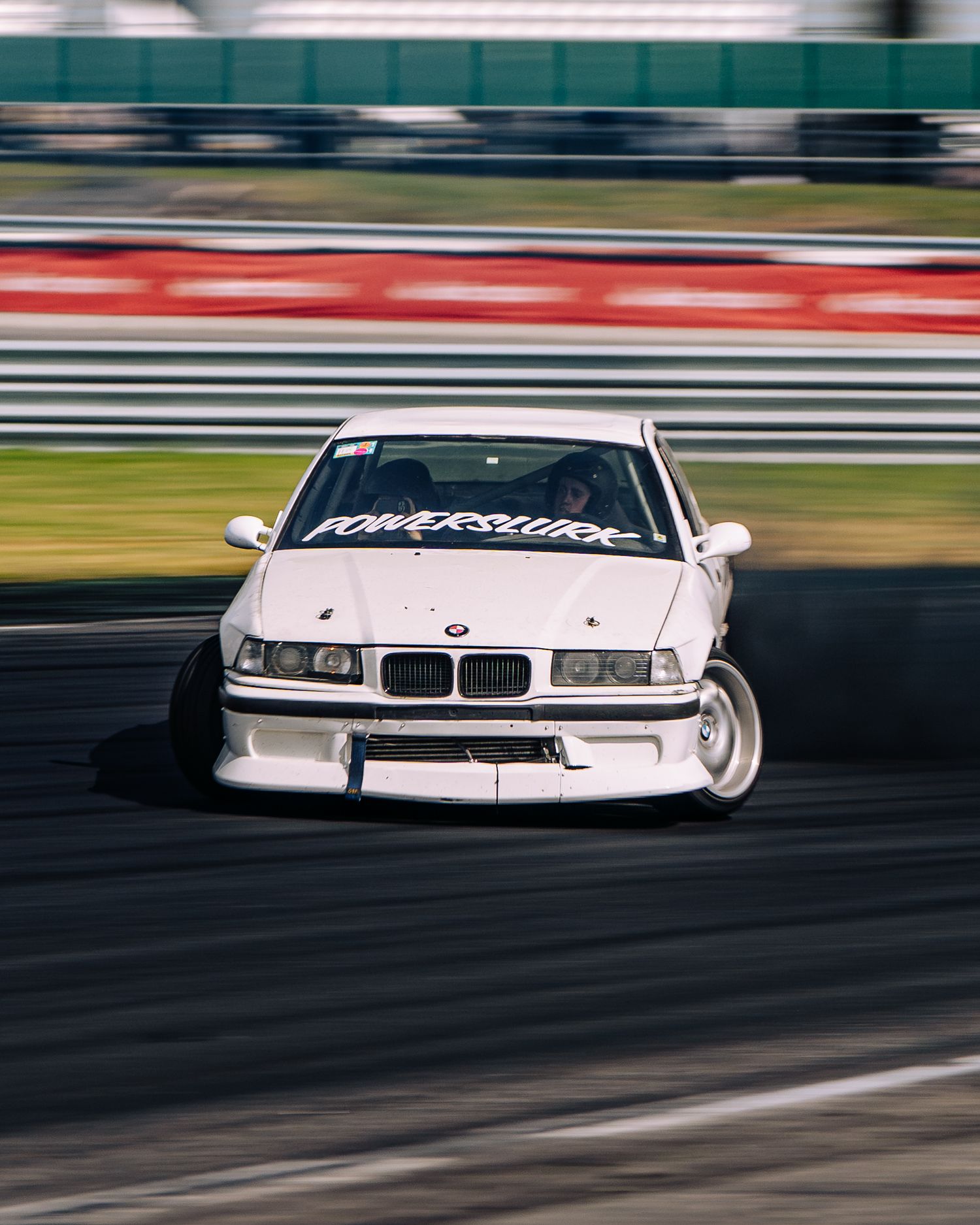 White BMW race car drifting on a racetrack with motion blur effect showing high-speed action.