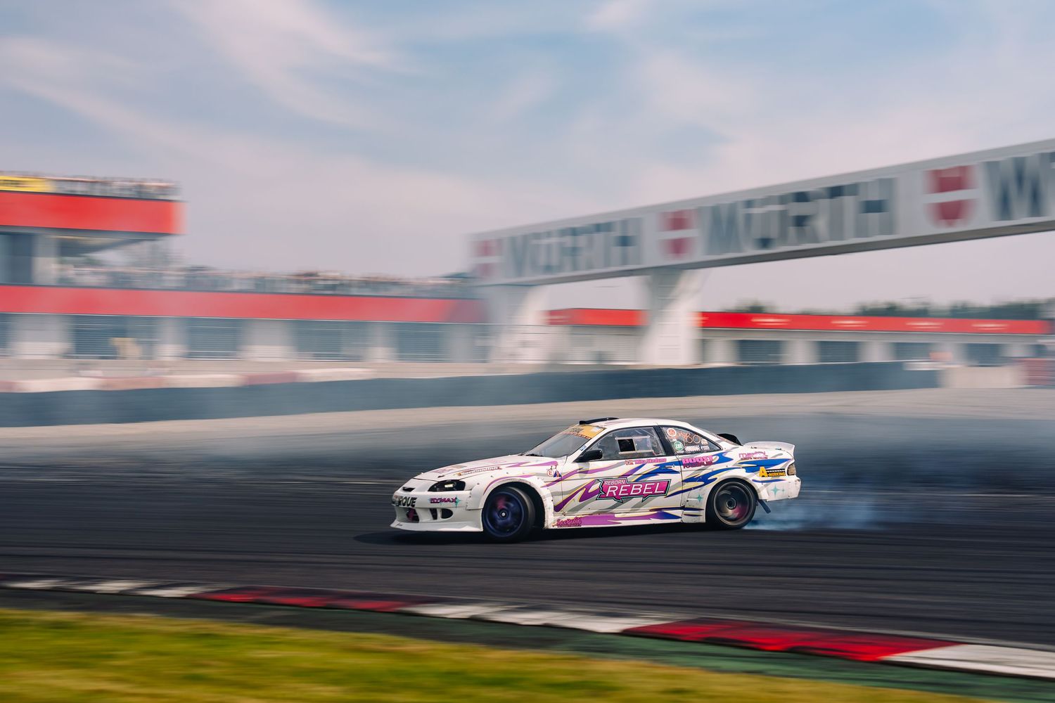 White BMW drift car creating smoke while drifting on a race track during a motorsport competition.