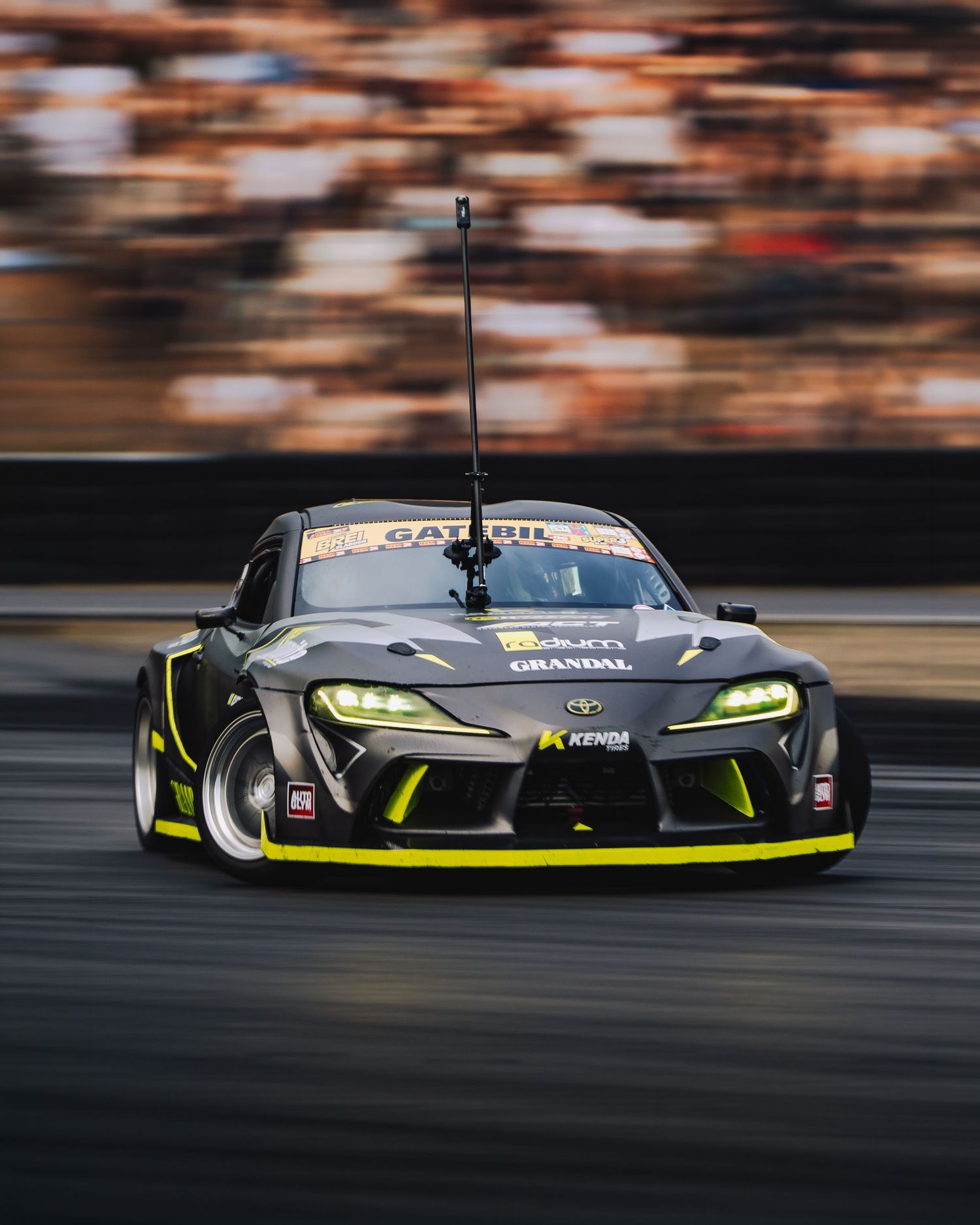 Black racing car with neon yellow accents speeding on track with motion blur effect in panning shot.
