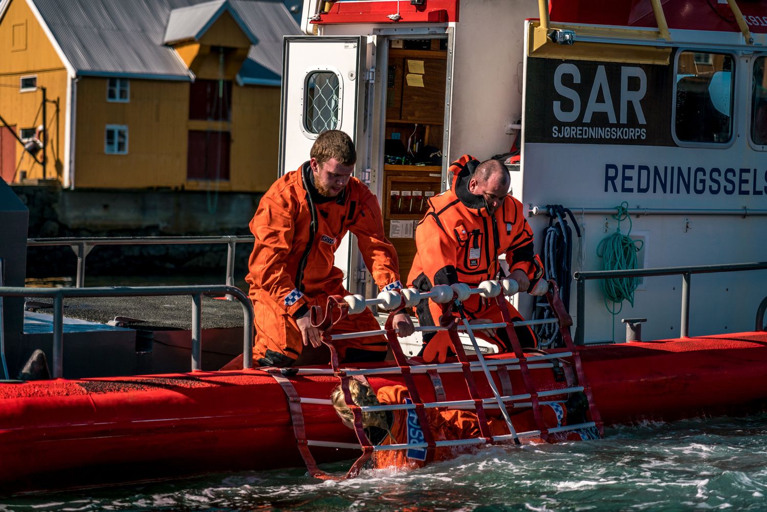 Rescue personnel in orange suits working on red boat equipment.