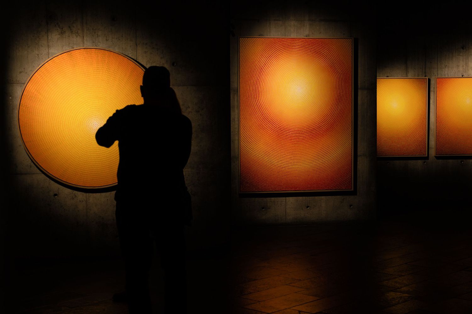 A dark silhouette stands before glowing orange circular artworks mounted in sequence.