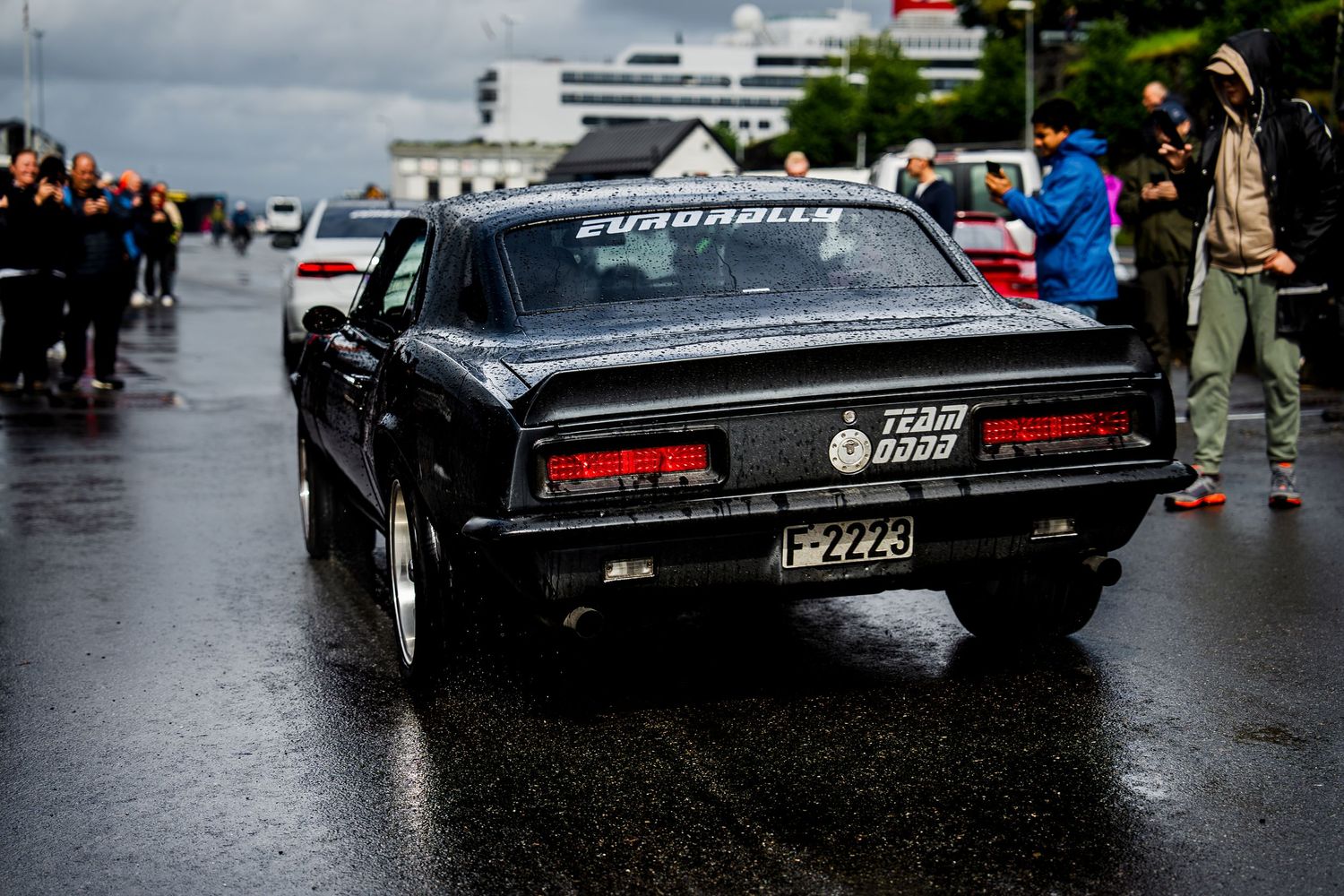 Classic black car shown in dramatic low angle photography on rainy asphalt.