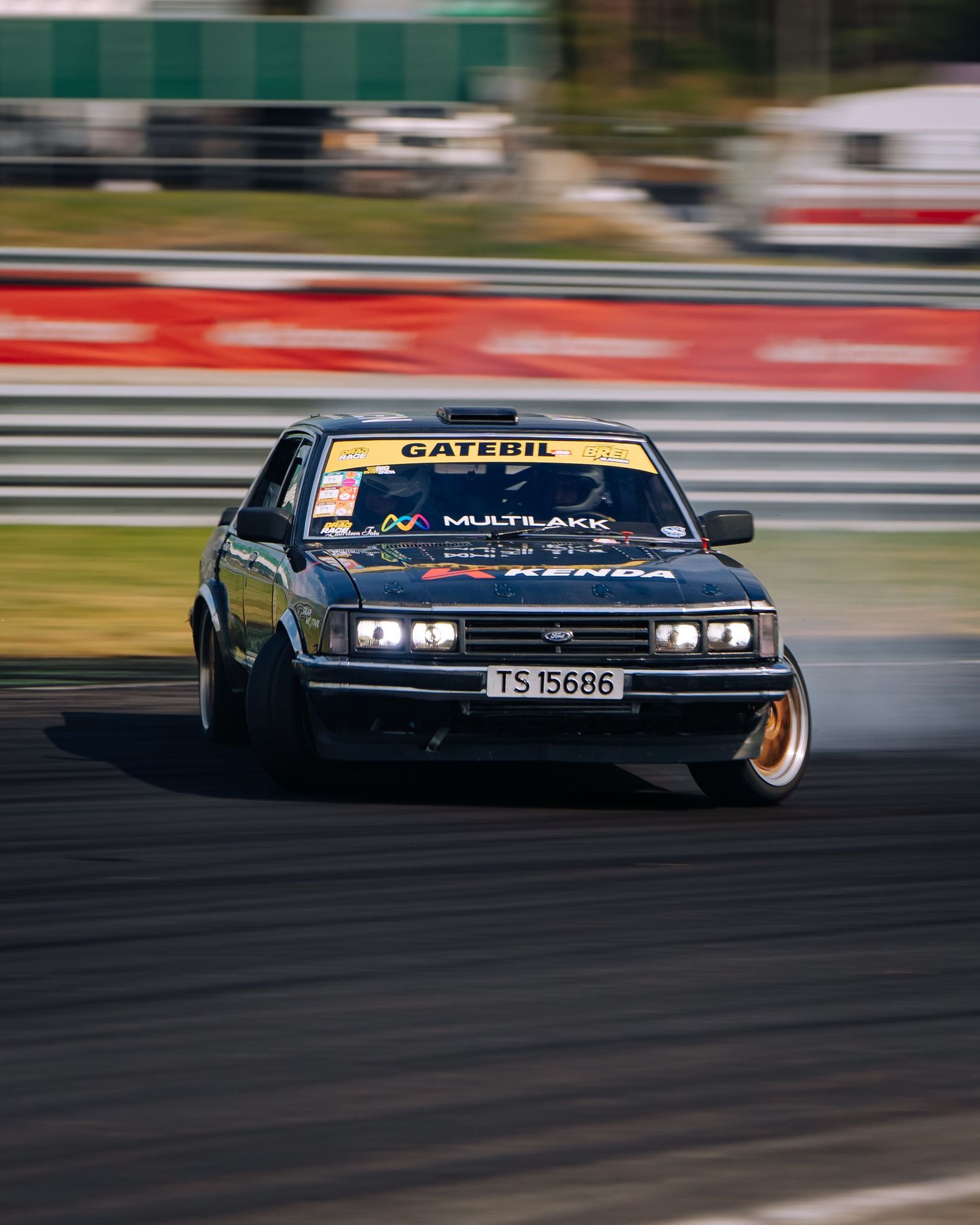 Two black race cars drift around a racetrack corner in a high-speed motorsport competition.