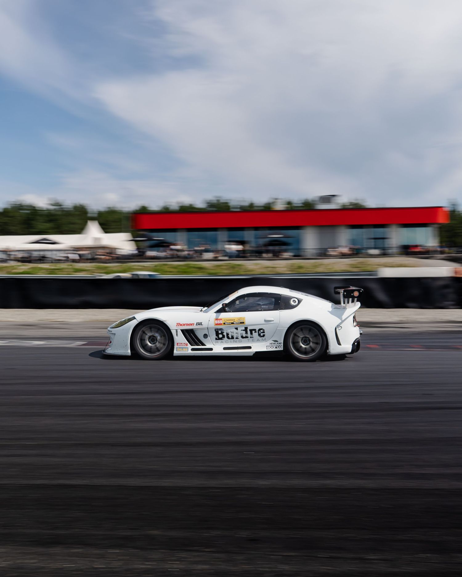 White Formula race car speeding along a racetrack with blurred motion against cloudy sky.