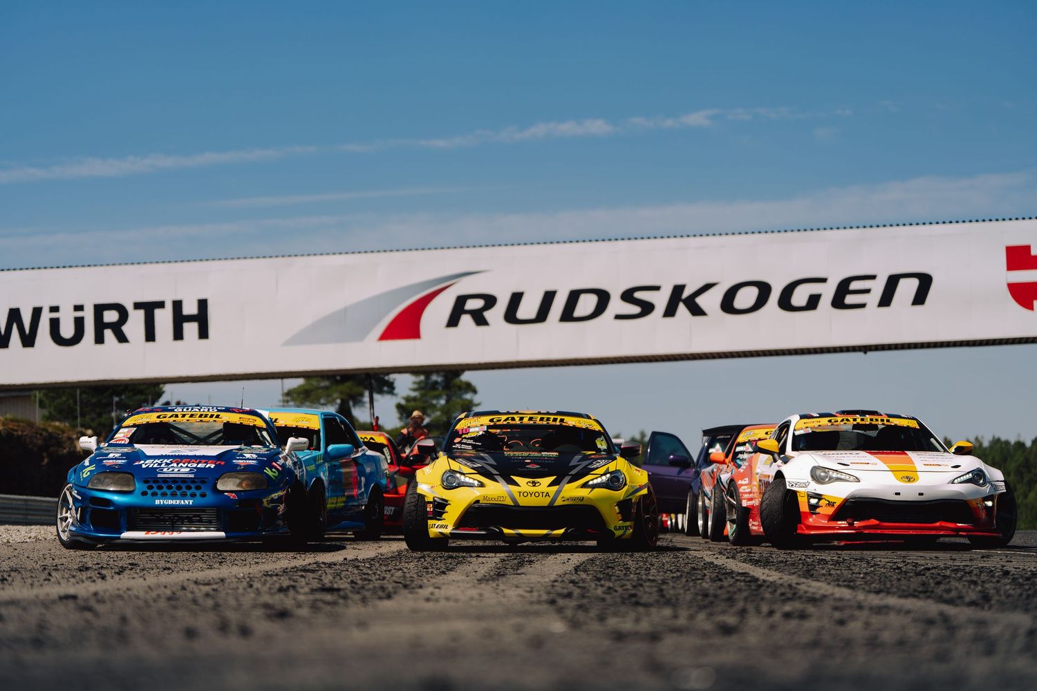 A row of colorful racing cars lined up on a track against a blue sky backdrop.