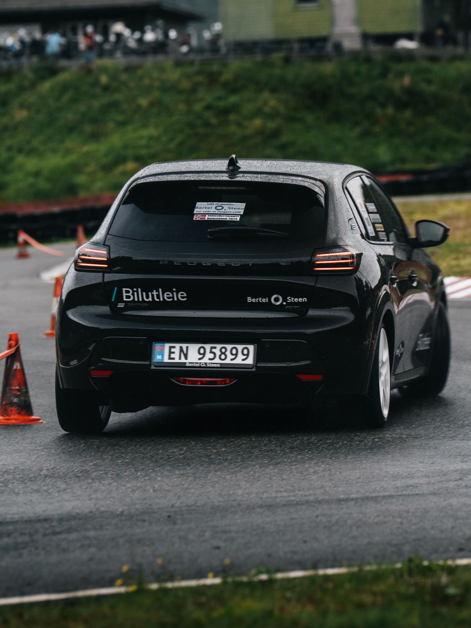 Black sports car drifting through orange traffic cones on a wet asphalt track during a performance driving event.