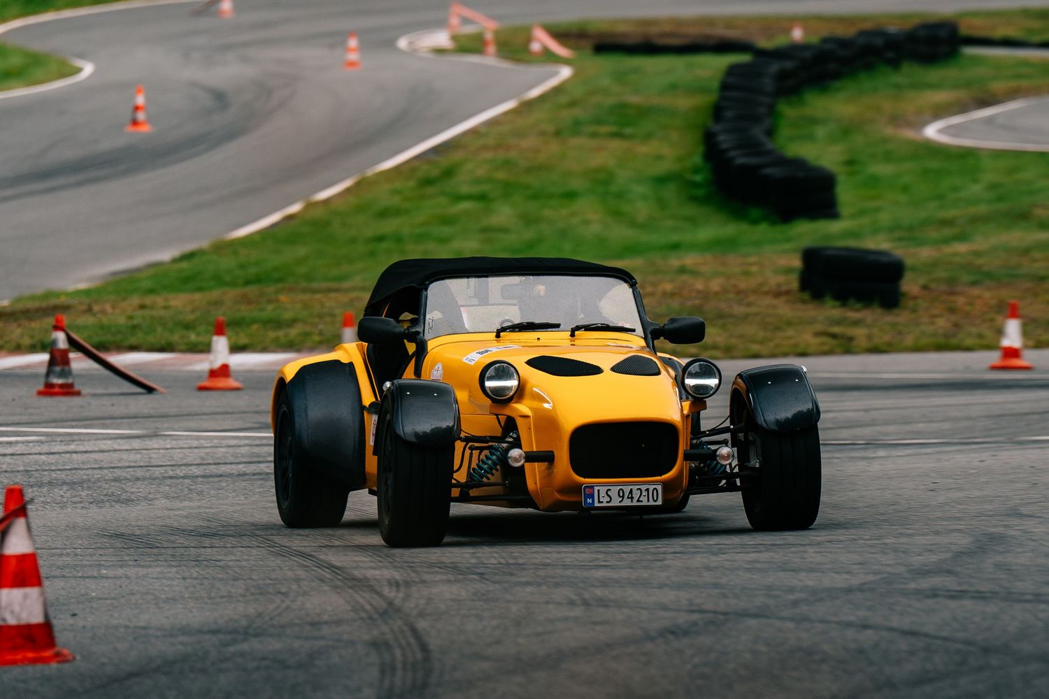 Yellow Caterham sports car navigating through orange traffic cones on a race track during autocross event.