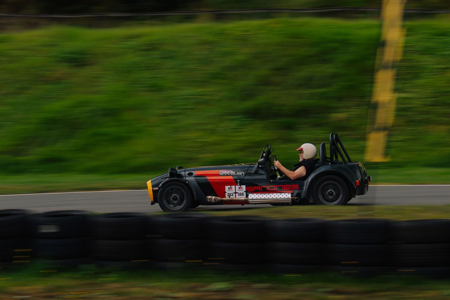 Red and black race car speeds along a winding track surrounded by lush green scenery.