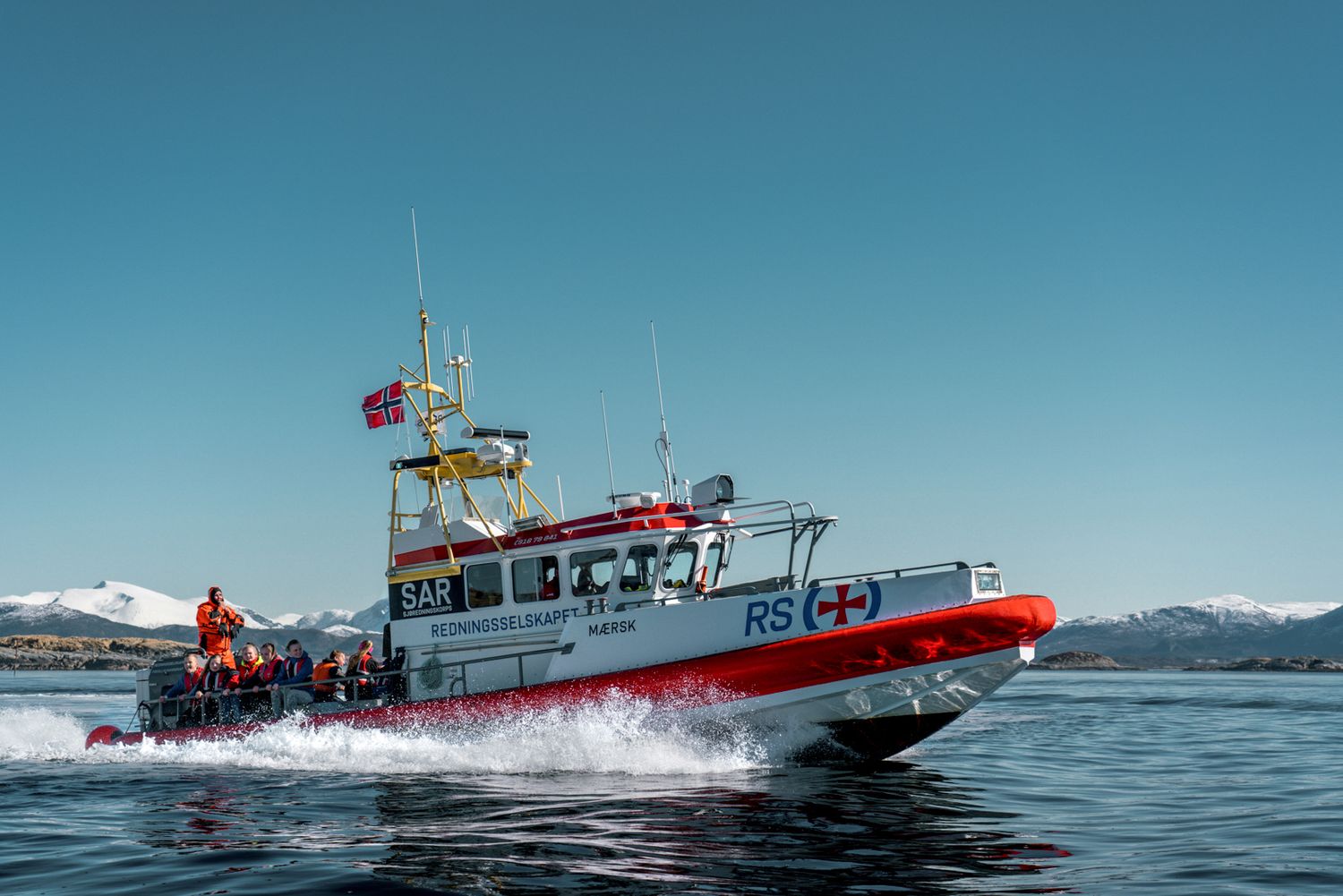 Rescue boat patrolling icy waters with Norwegian flag flying against blue sky backdrop.