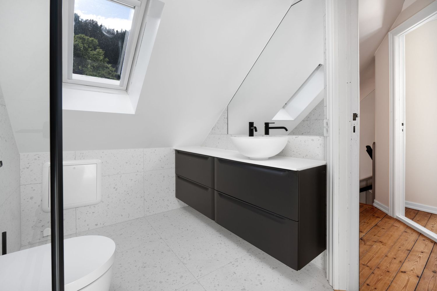 Sleek bathroom featuring dark floating vanity, white walls, and skylight in attic space.
