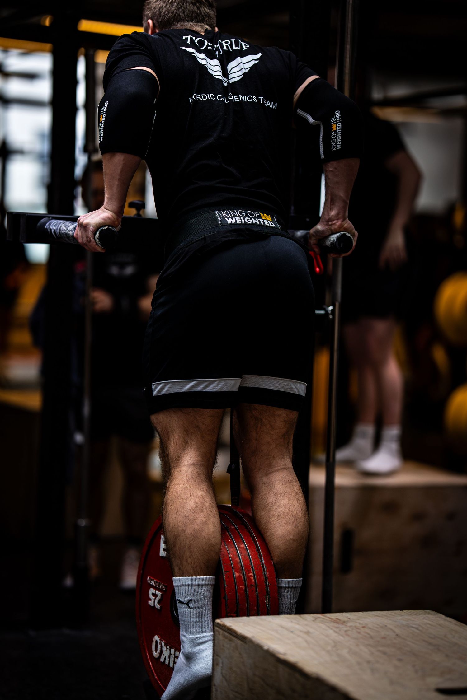 Close-up of an athlete's legs and feet during a CrossFit workout wearing black shorts and red weightlifting shoes.