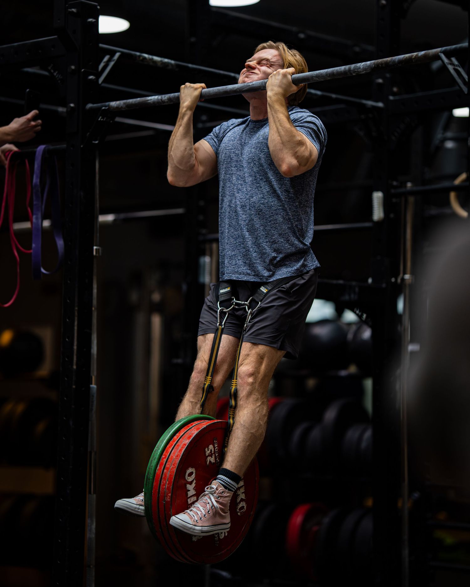 Athlete performs pull-up while balancing on weight plates in dark gym setting.