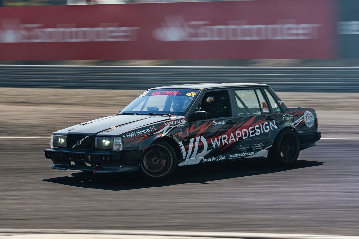 Multiple race cars speed around a racetrack during a competitive motorsport event.