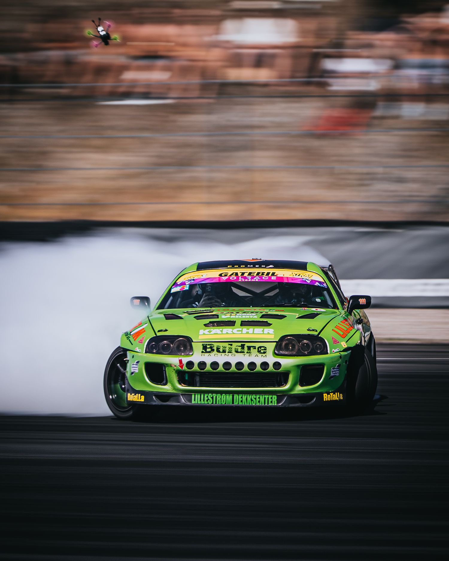 A green race car drifts on the track creating motion blur during a motorsport competition.