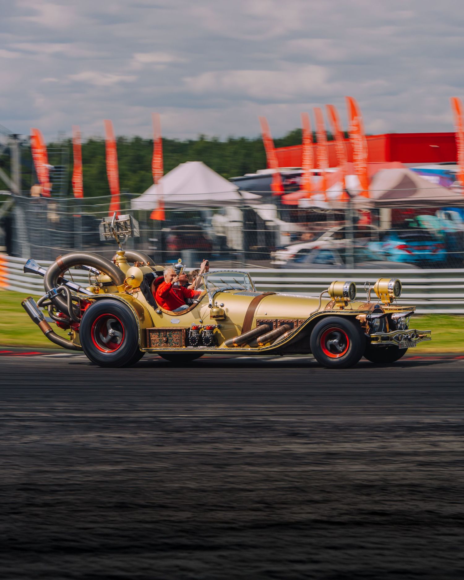 A gold jet-powered car races along a racetrack with flames shooting from its exhaust during a motorsport event.