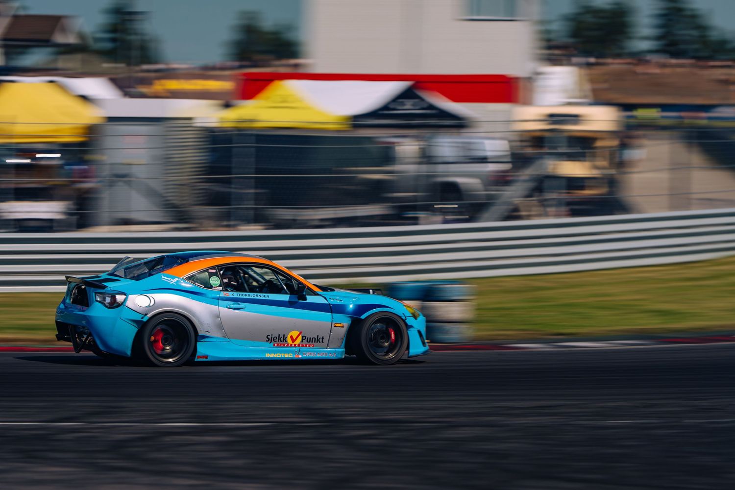 Drift cars slide sideways around a racetrack with colorful smoke trails and barriers in the background.
