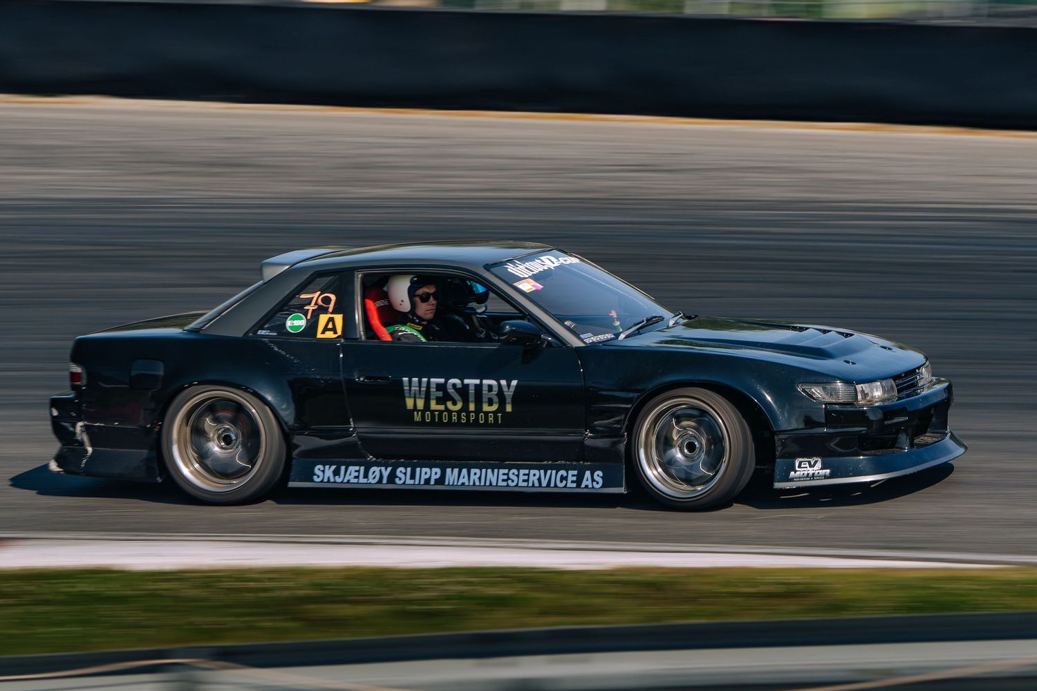 Black racing car speeds along a racetrack during a competitive motorsport event.