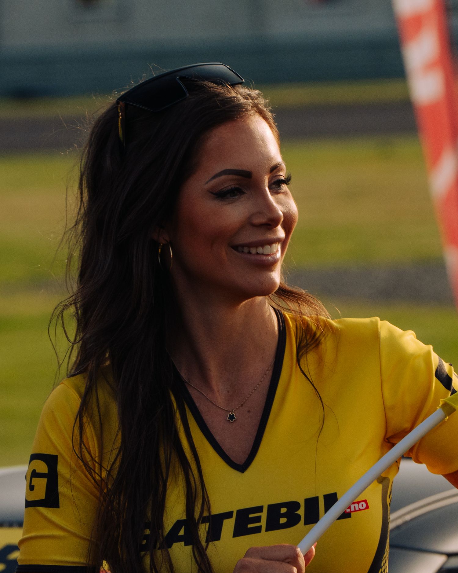 Female model in yellow motorsports promotional uniform smiles during outdoor event.
