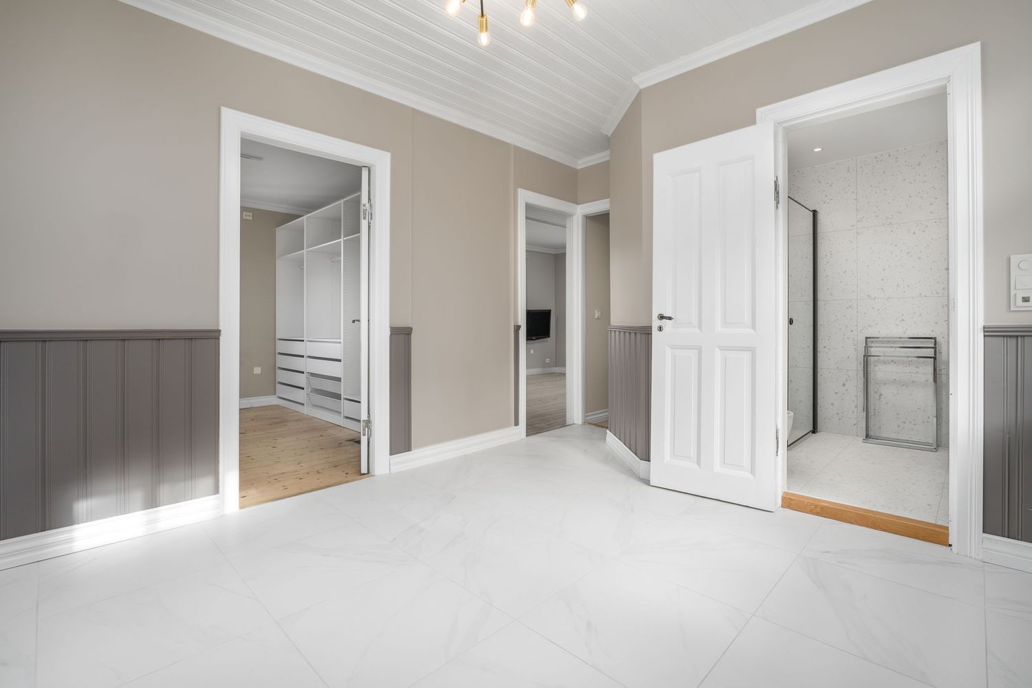 Spacious room with white doors, beige walls, and grey wainscoting panels.