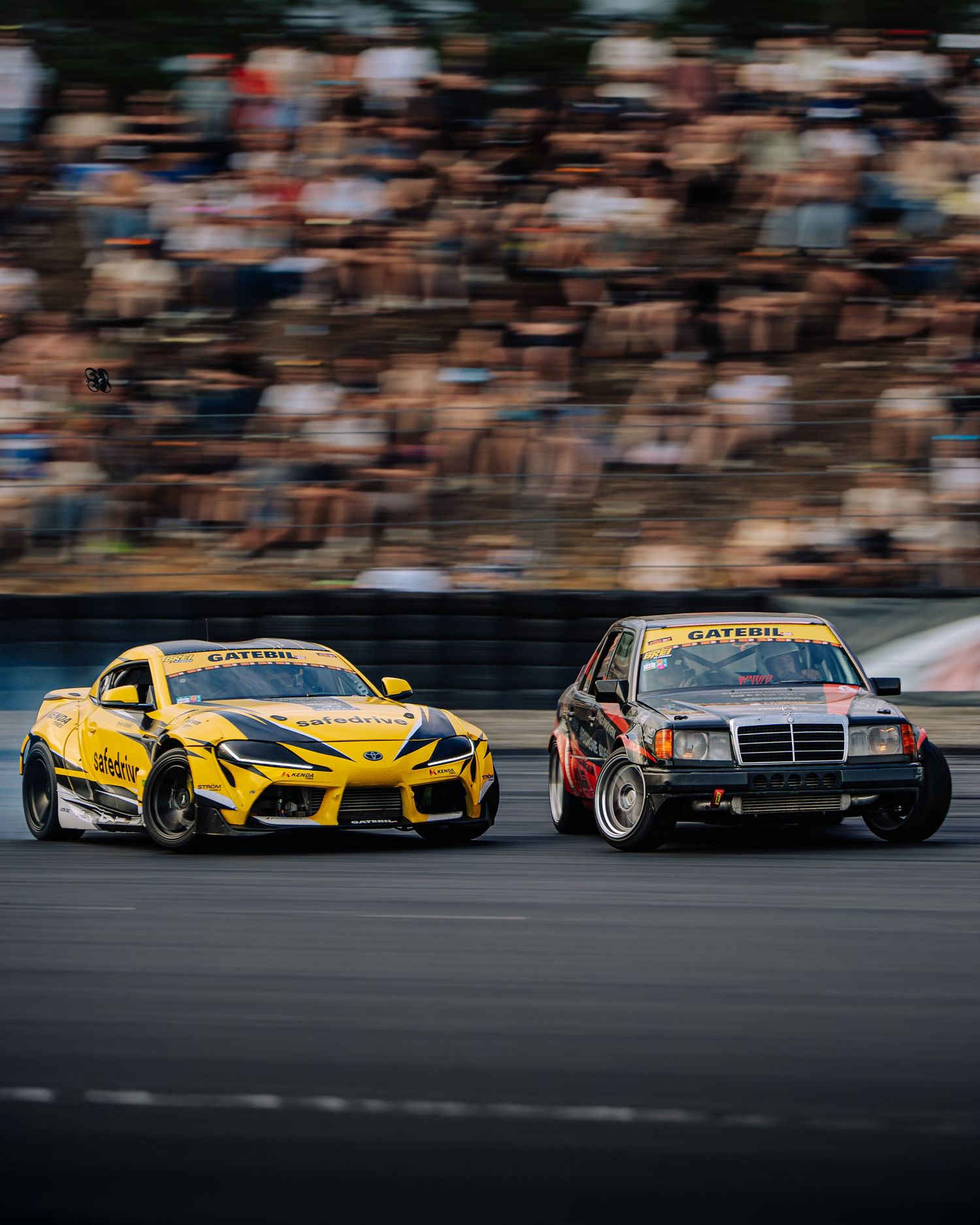Professional drift cars race side by side on a track during an intense competition event.