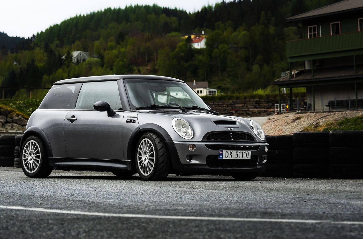 A collection of gray and silver sports cars parked on asphalt with forest and mountains in the background.