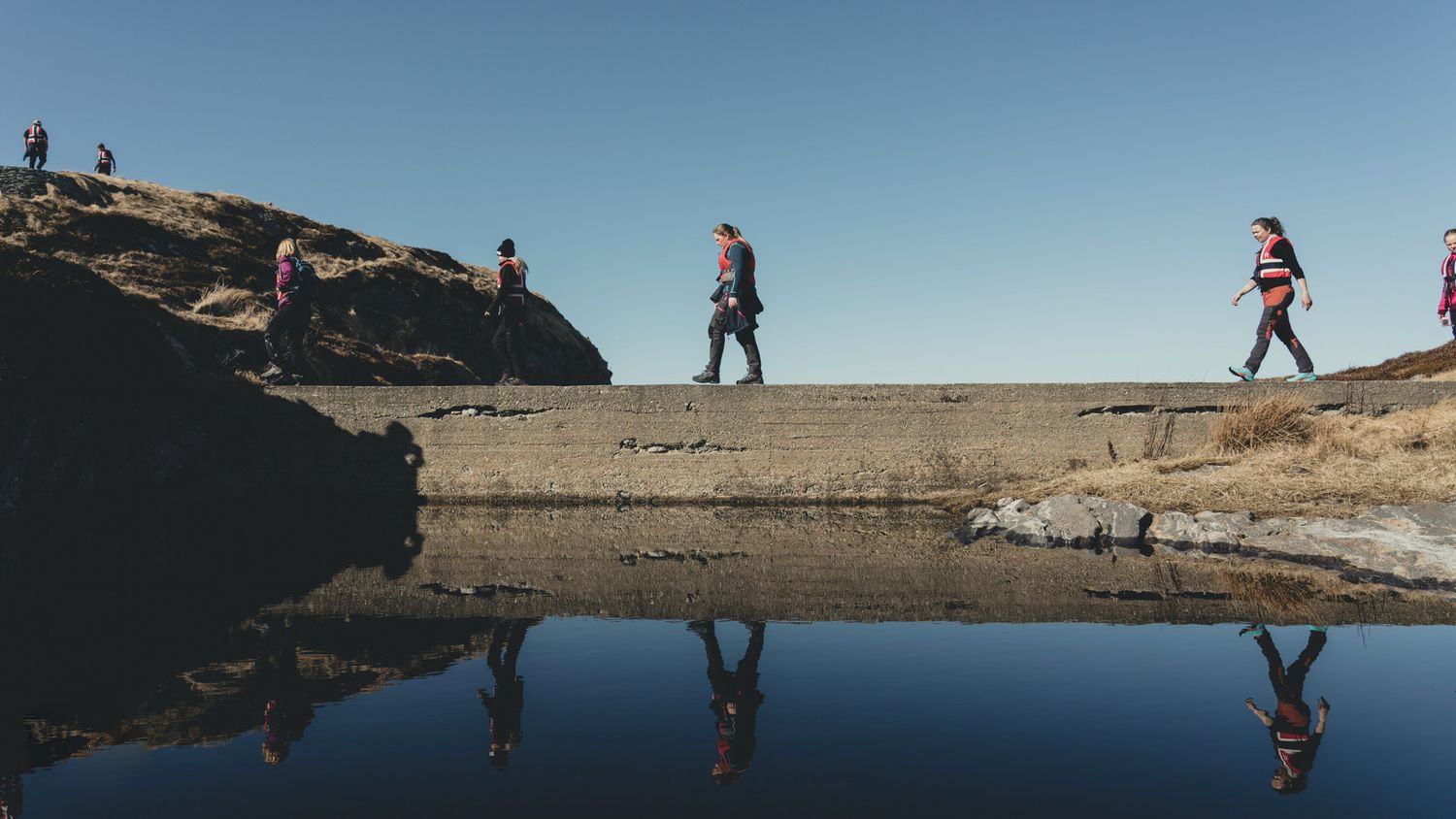 Silhouettes reflected in still water against rocky coastal landscape.