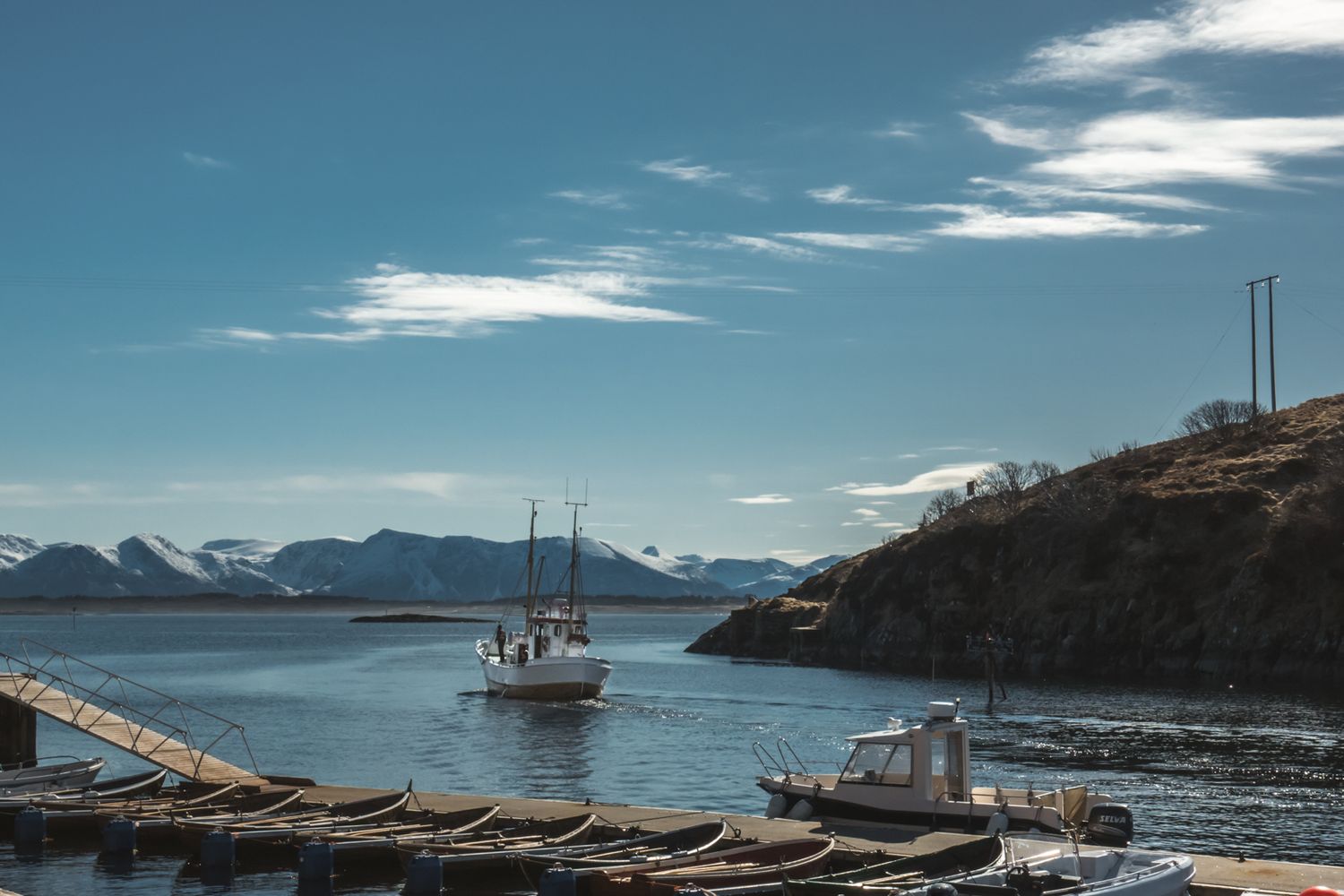 Fishing boat navigates through fjord waters surrounded by rocky cliffs and mountains.