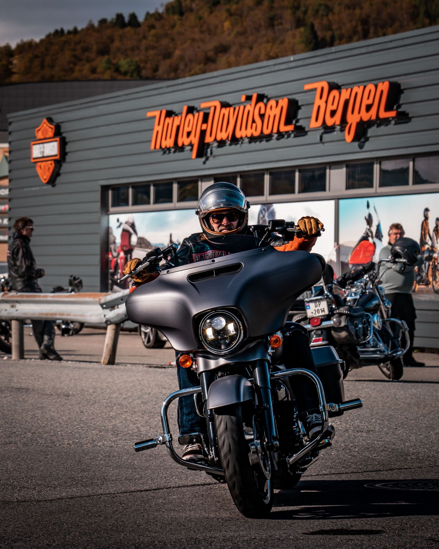 Motorcycles and riders gathered outside Harley-Davidson dealership with orange signage.