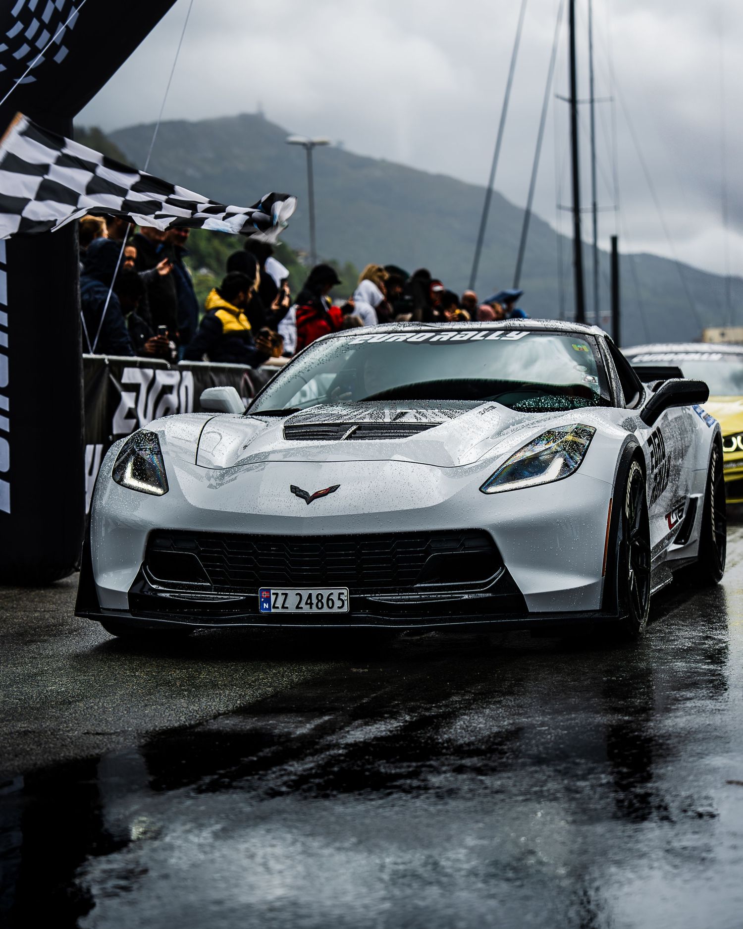 Silver Chevrolet Corvette passing under Eurorally finish arch during wet race conditions.