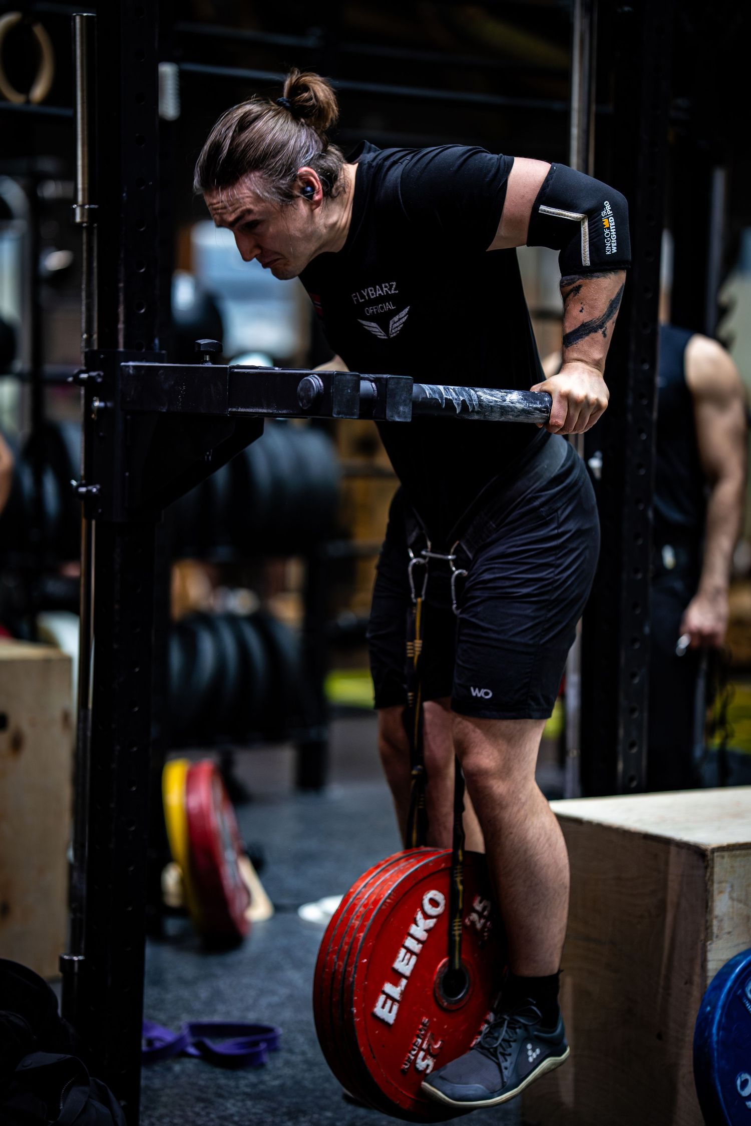 Athlete performs weighted dips at a CrossFit gym with red Eleiko weight plates visible in dark setting.