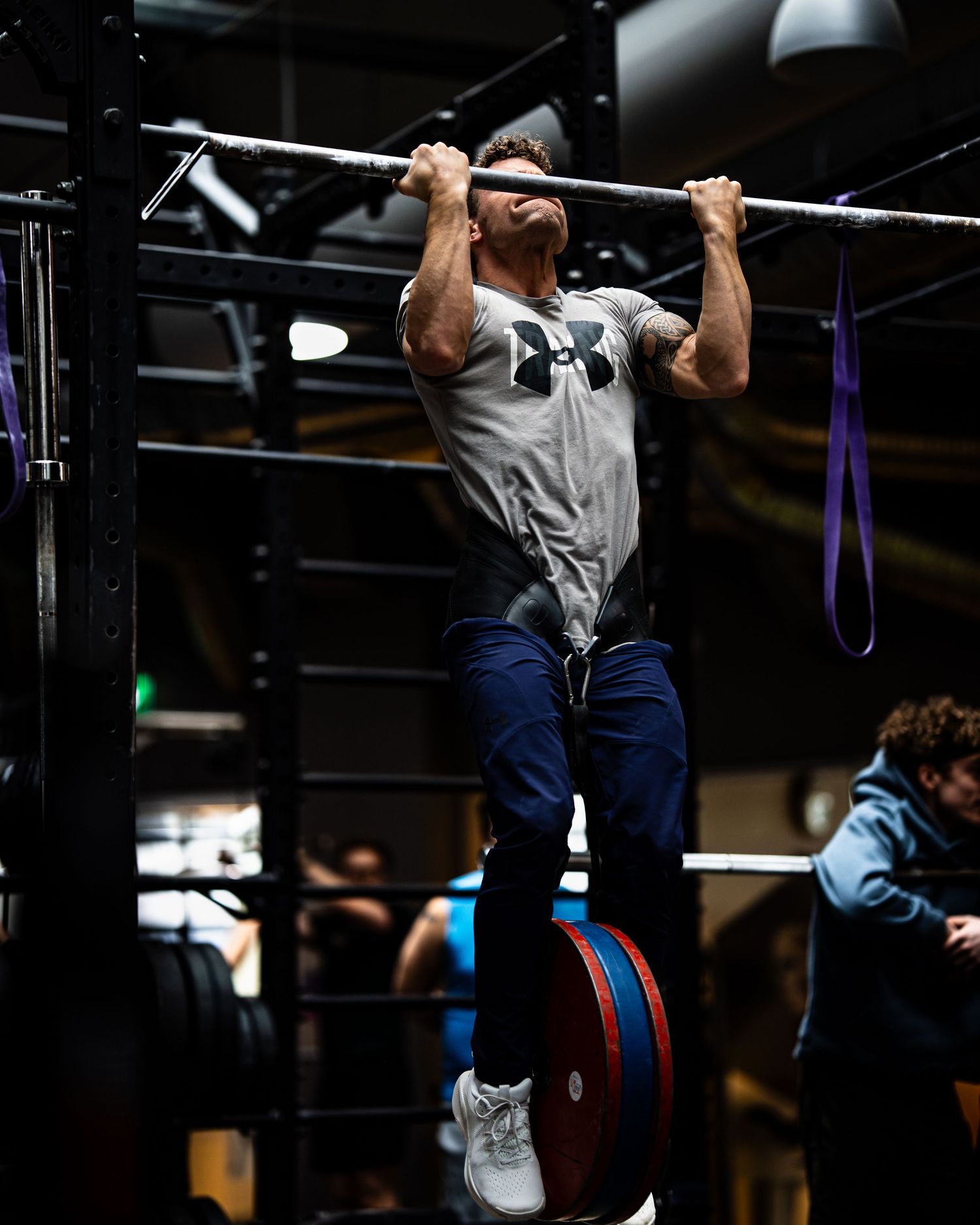 Athletes practicing pull-ups on gym bars in a dark training environment.