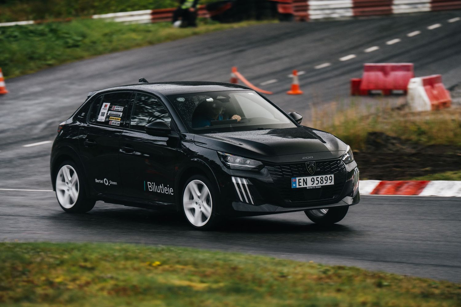 Black sports car drifting on a race track with orange safety cones and barriers visible.