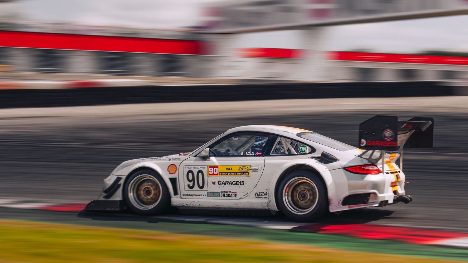 Racing car speeds past red and white curbing on a professional motorsport track during competition.