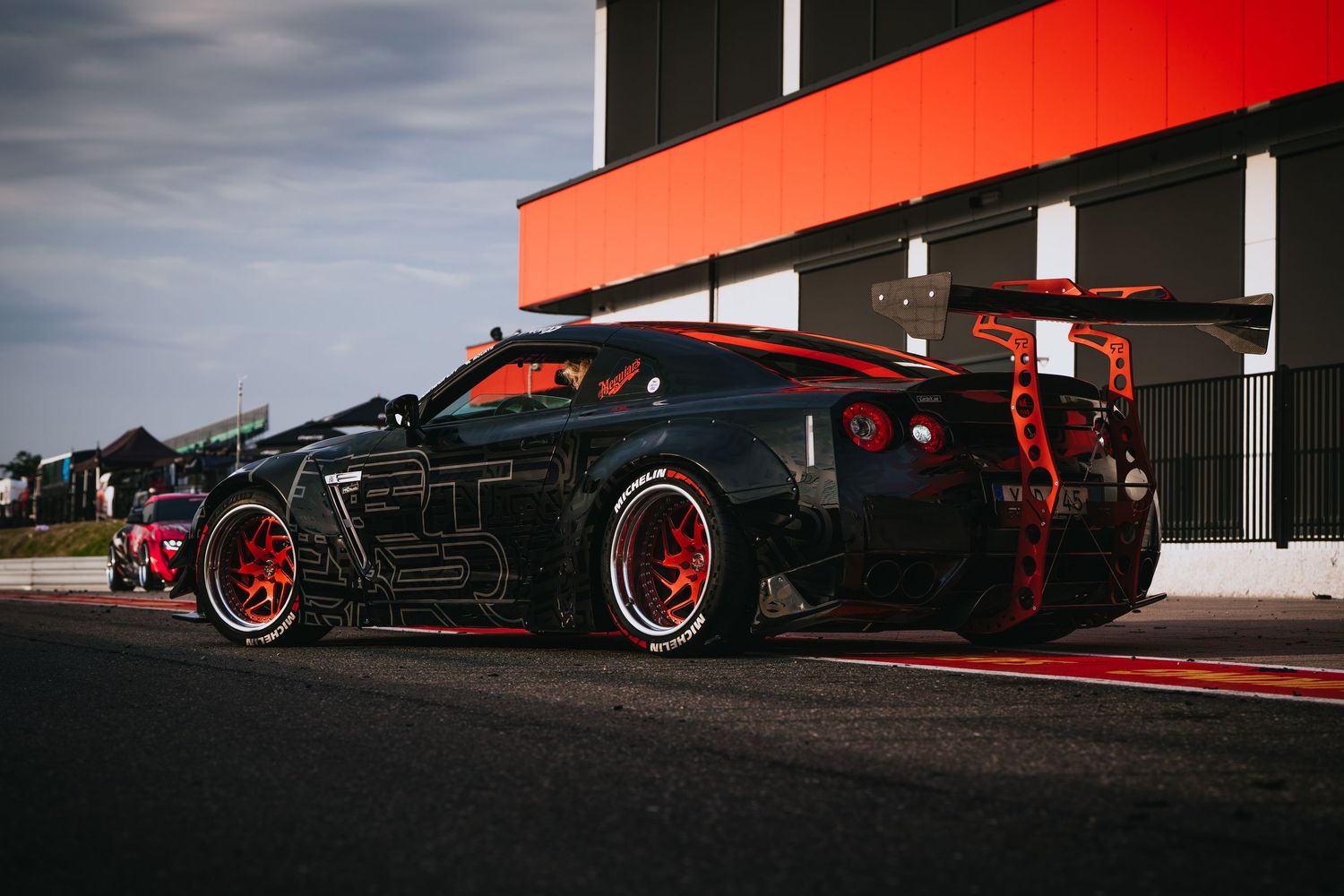 A collection of modified sports cars with red accents parked in a row at a car meet event.