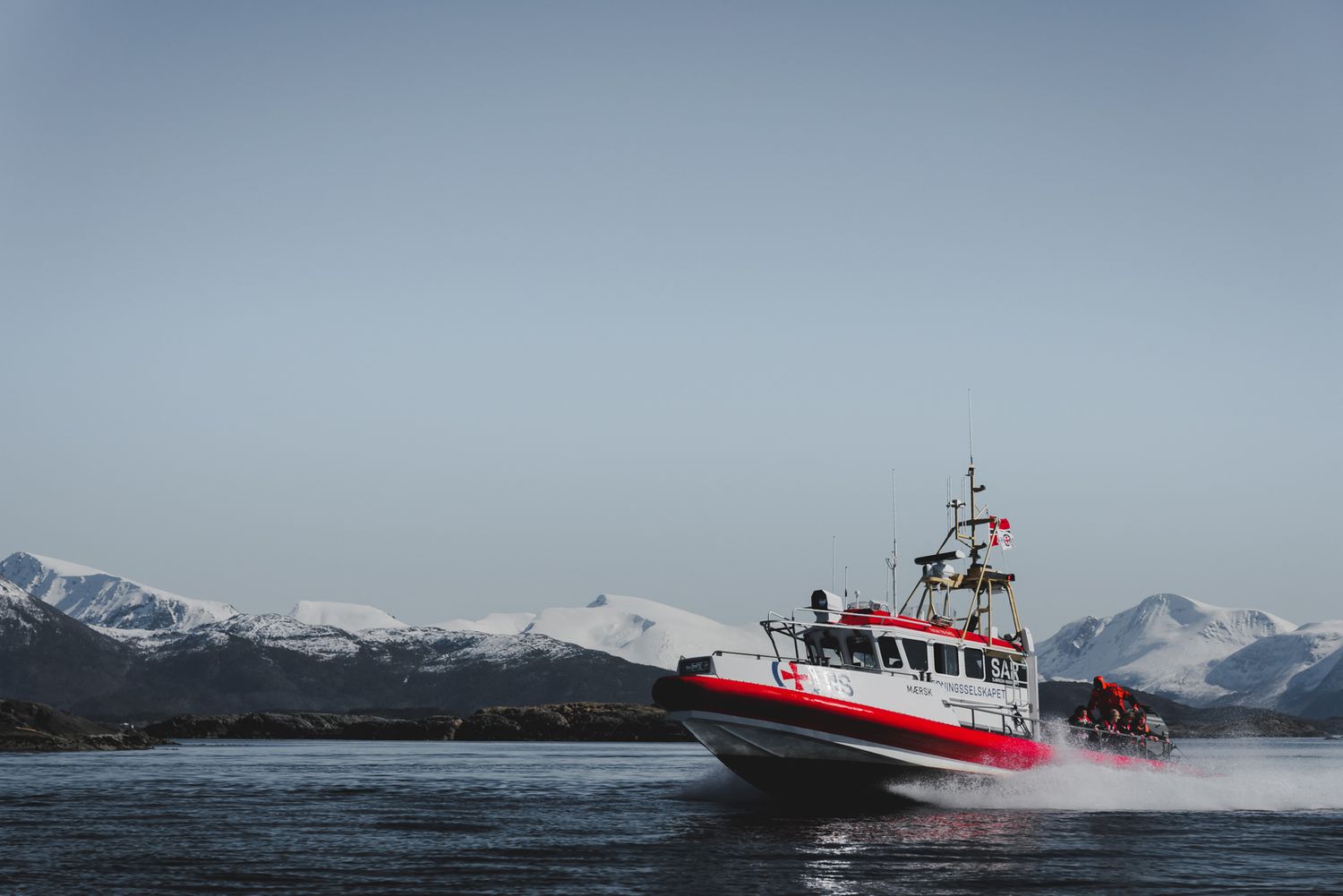 Search and rescue boat speeding through rough arctic waters near mountainous coastline.
