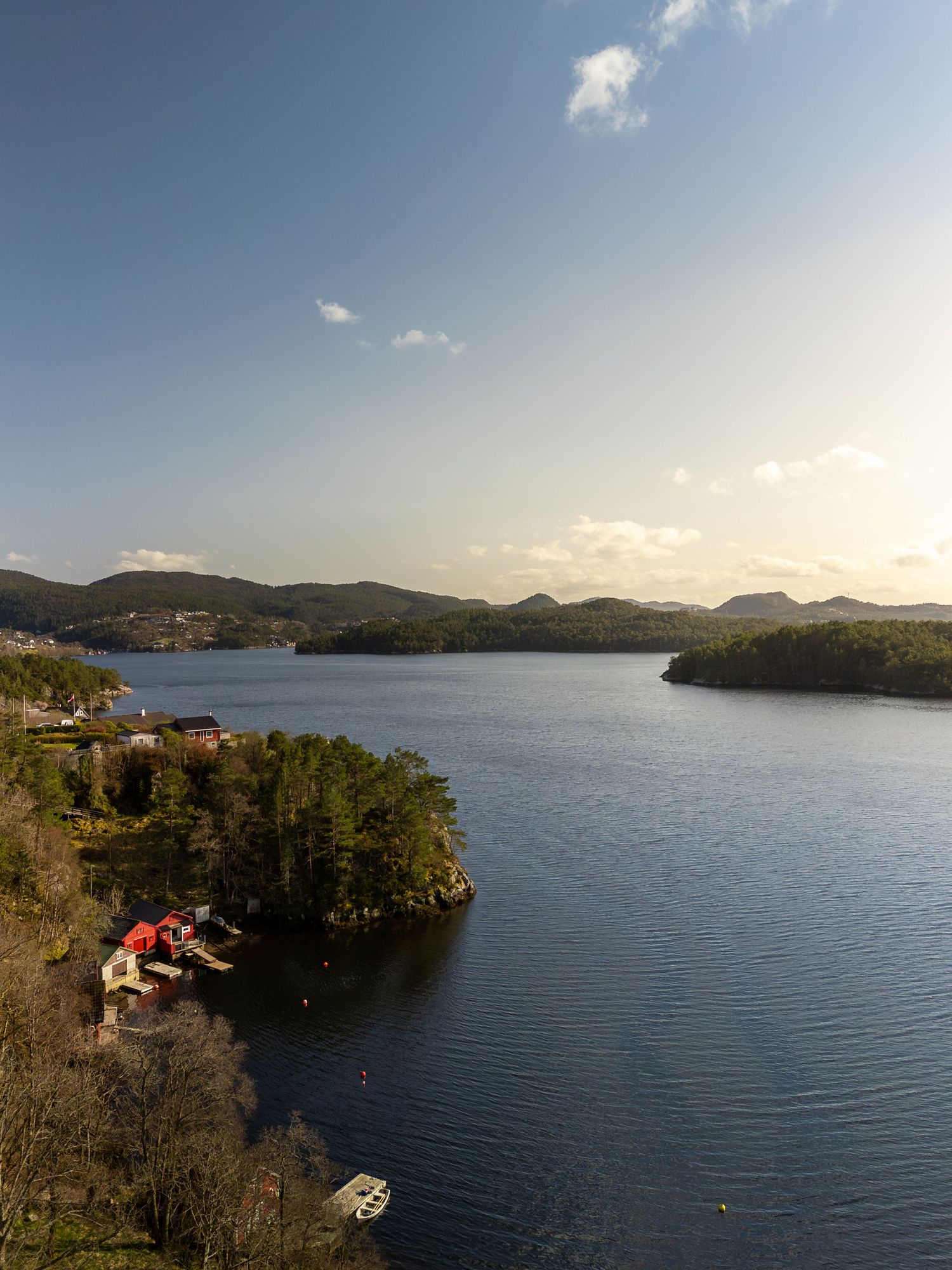 Scenic view of a tranquil fjord surrounded by rolling hills and trees with waterfront cottages nestled along the shoreline.