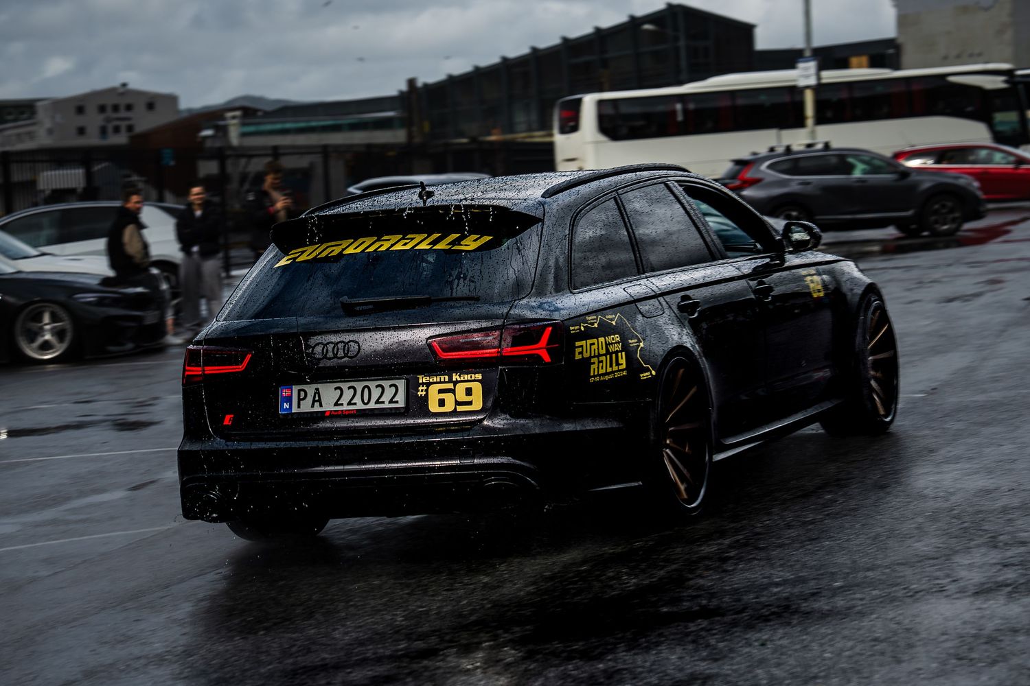 Row of luxury black cars parked on wet pavement under stormy skies.