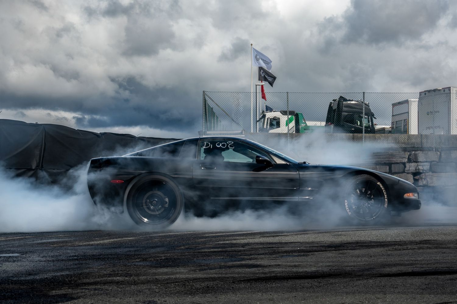 A series of cars performing burnouts and drifting maneuvers creating clouds of tire smoke on a track.