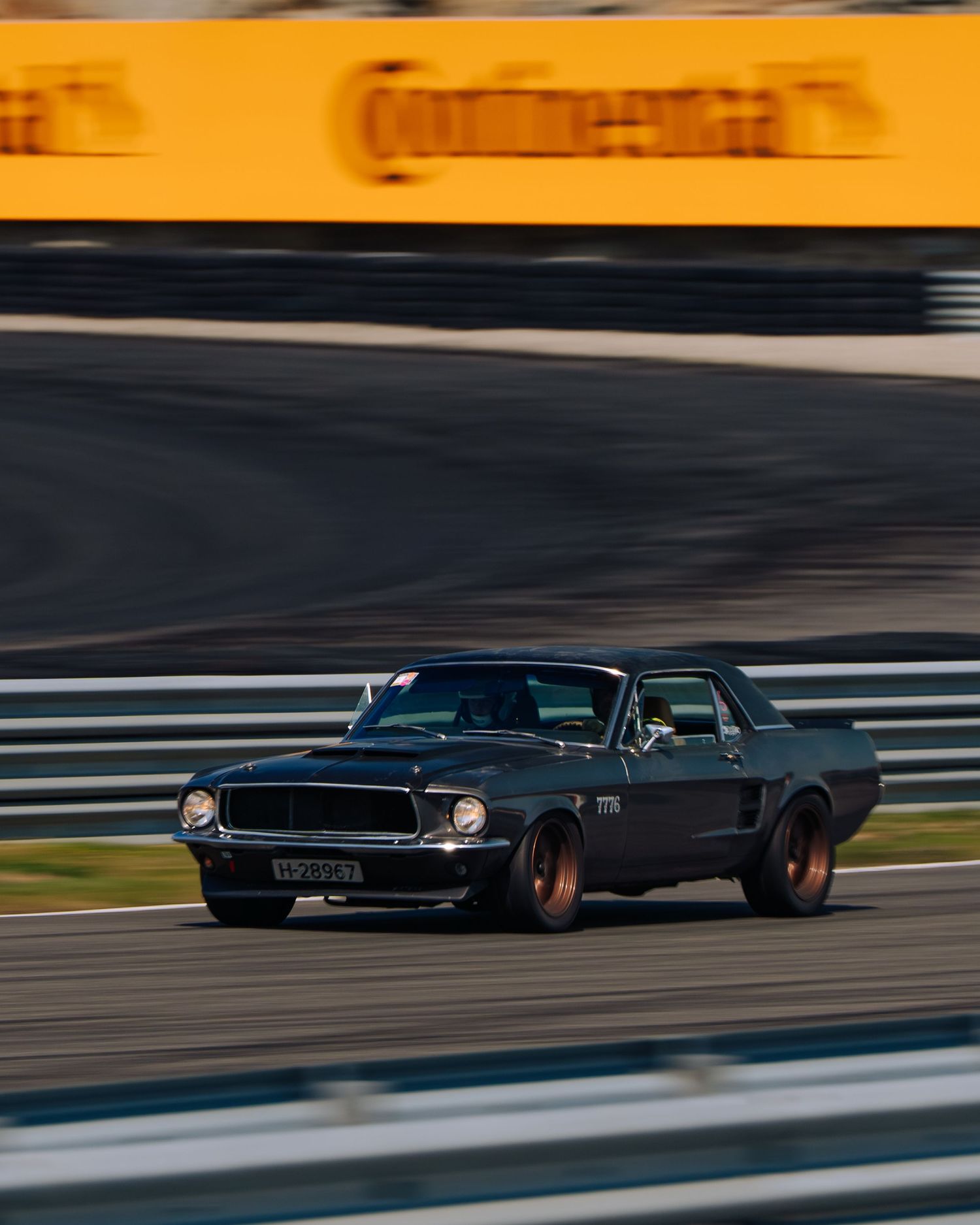 A sleek black vintage car races along a curving racetrack during sunset creating a dramatic silhouette effect.