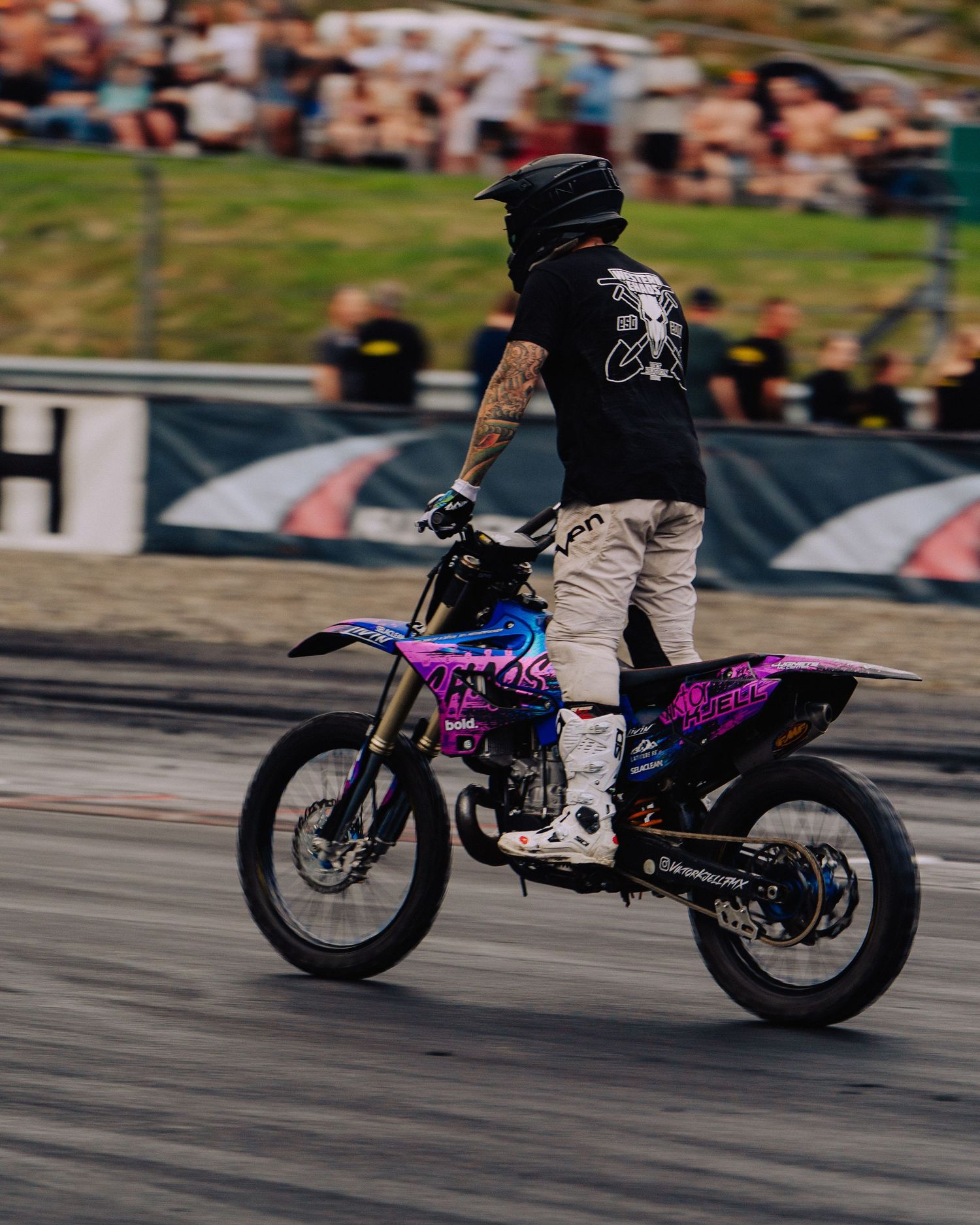 A purple motocross bike performing a high-speed run on a racetrack with spectators in the background.