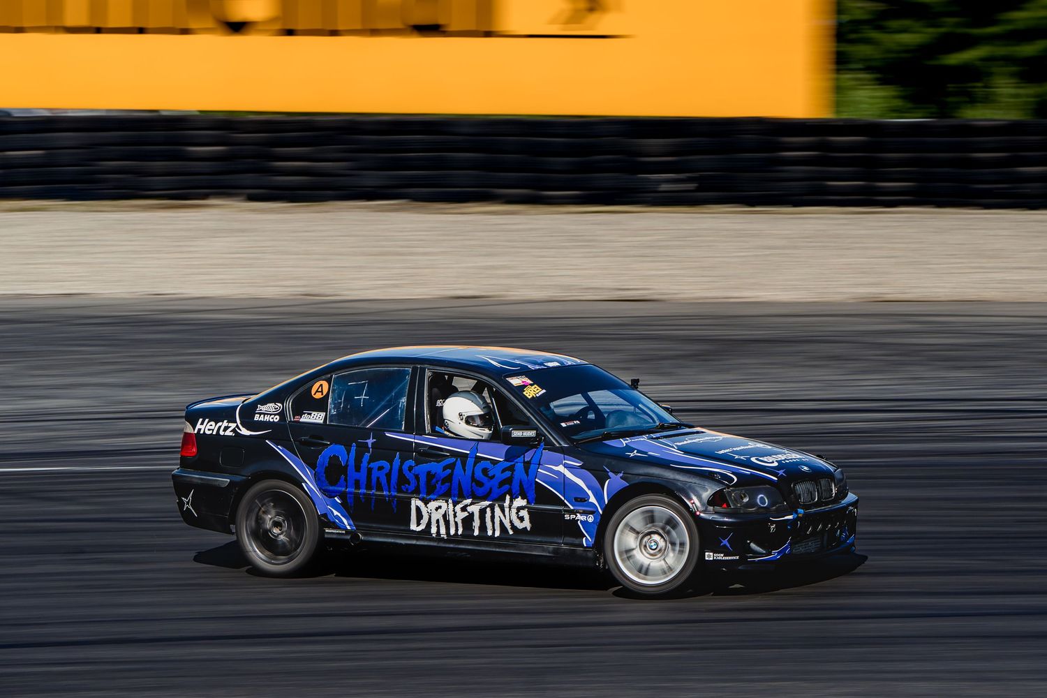 Blue drift car slides sideways on racetrack during competitive motorsport event.