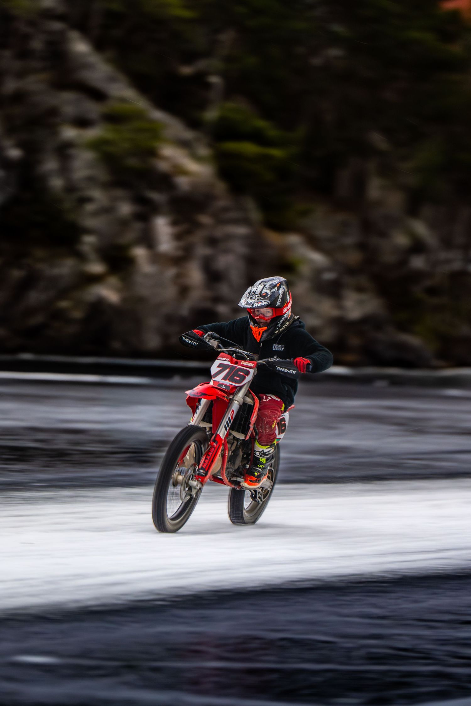 A red motorcycle performs a dramatic hydroplaning stunt across a lake surface in a sequence of action shots.