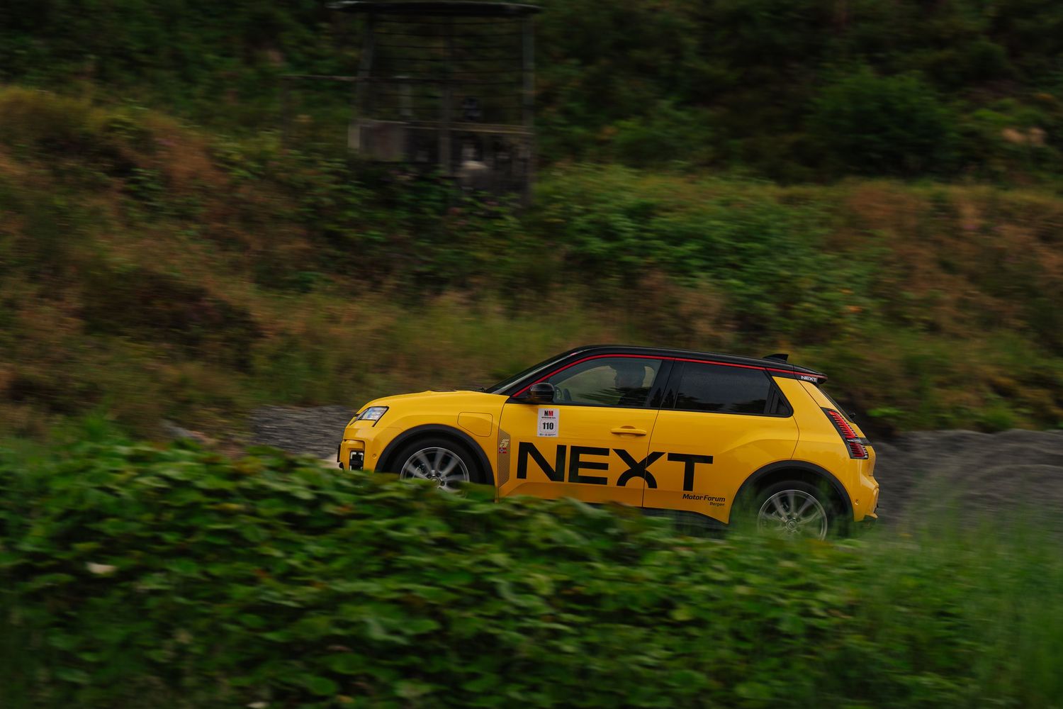Yellow sports car drives along a winding forest road during autumn season with green foliage in background.