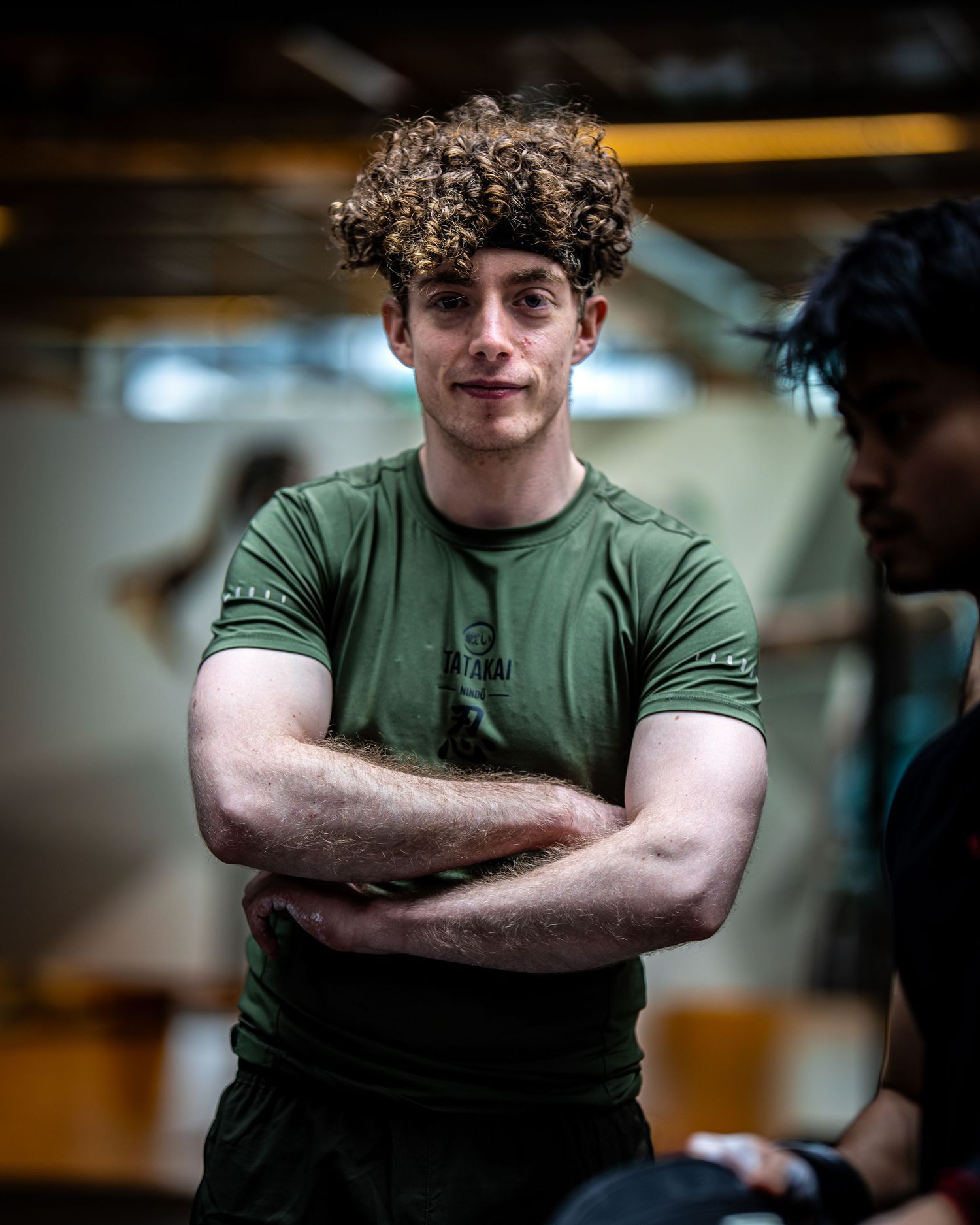 Athlete in green t-shirt posing with crossed arms in gym environment.