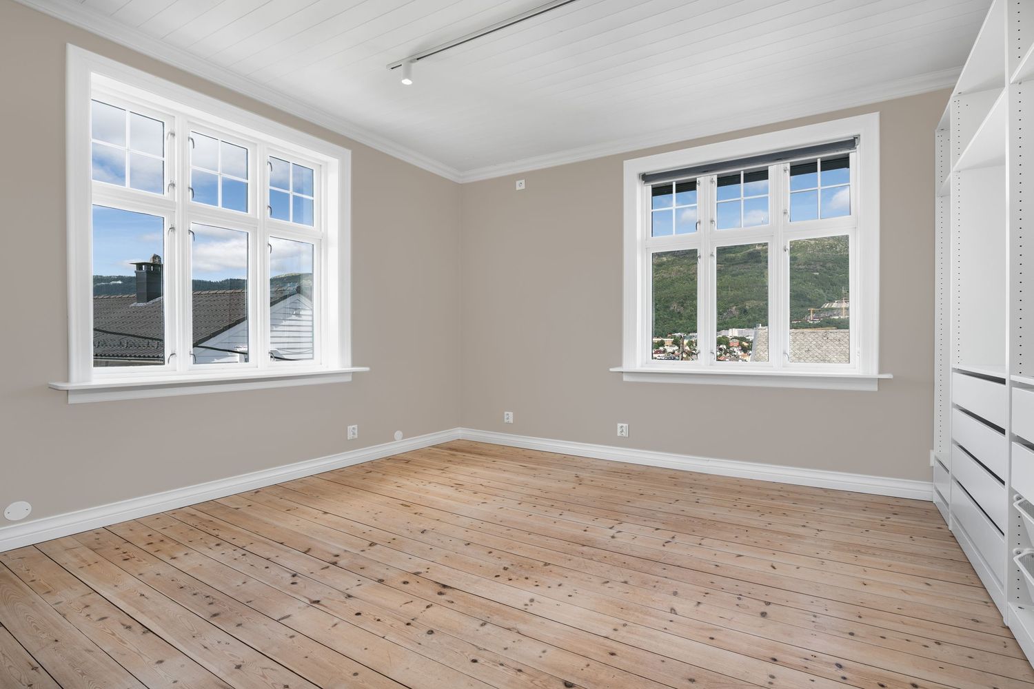 Airy room featuring tall windows, light beige walls, and pristine wood flooring.