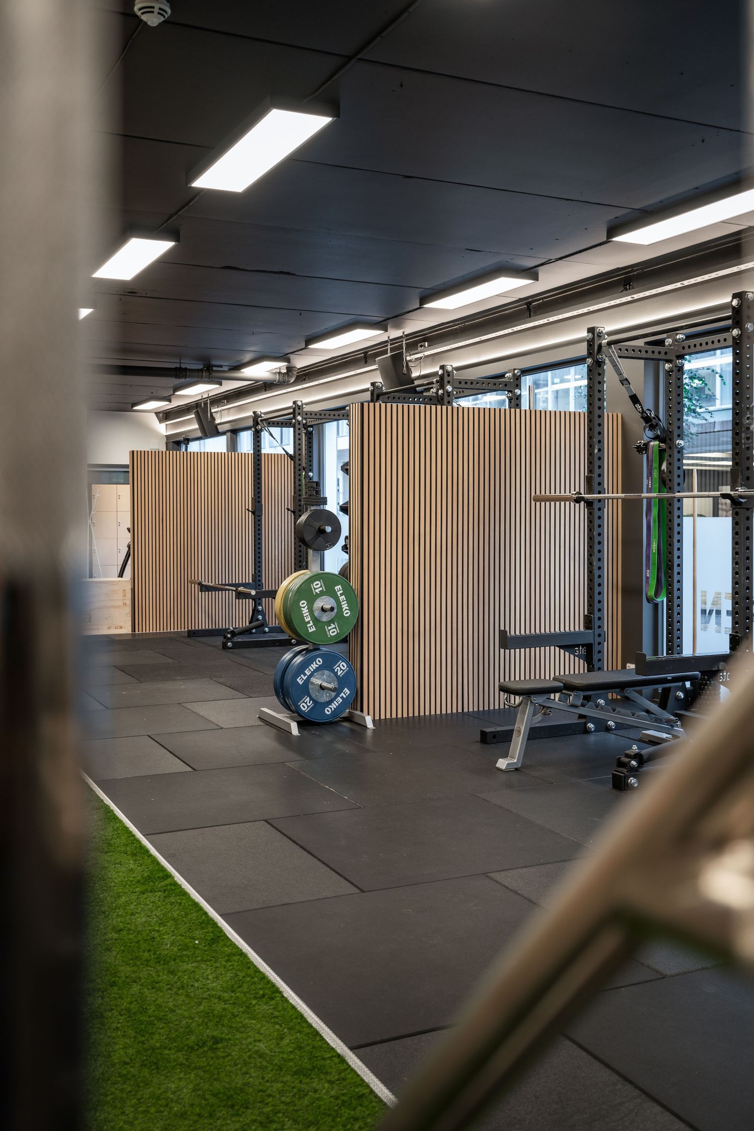 Modern gym interior with wooden dividers, exercise equipment and artificial turf flooring.