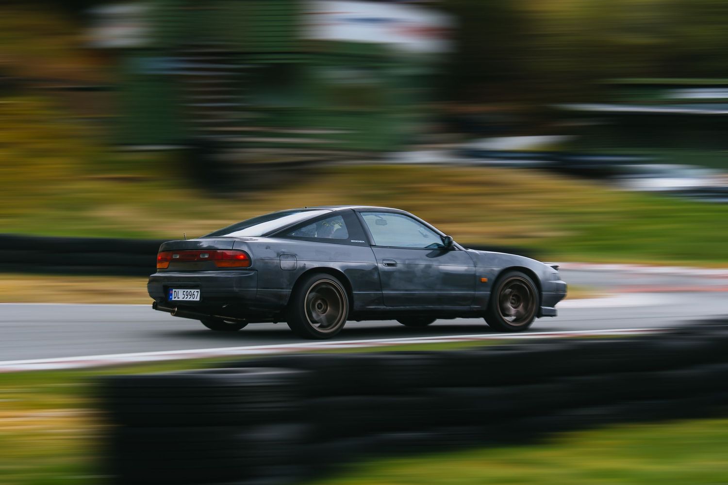 A dark colored sports car speeds through a motion-blurred forest road in a series of action shots.