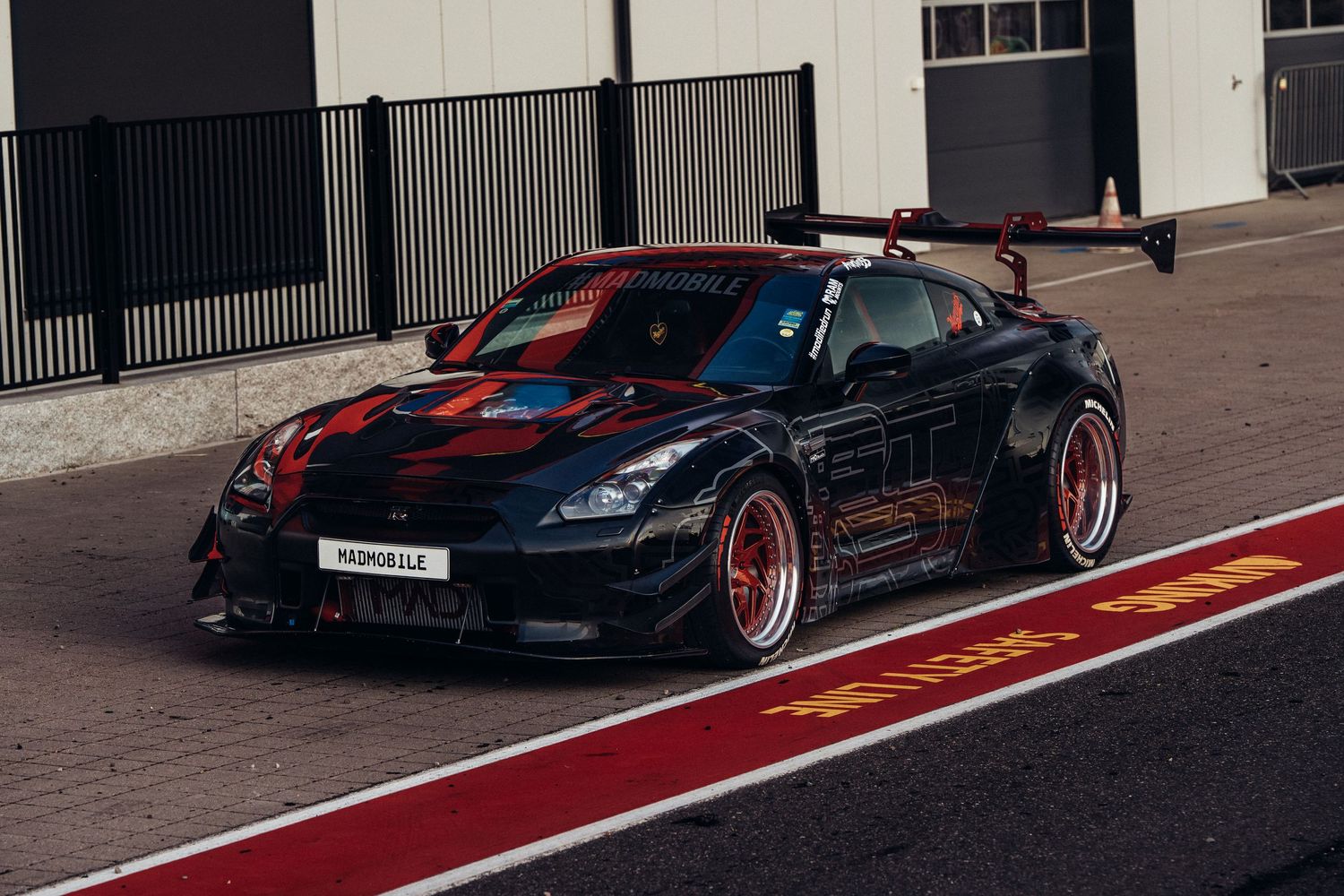 Modified black sports car with red racing stripes and custom wheels parked on a red-lined street.