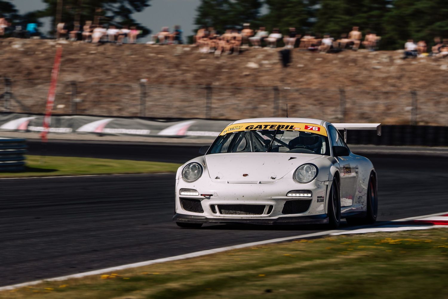 White Porsche race car speeds around a track during a competitive motorsport event at sunset.
